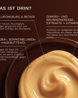 Eine goldene Cremetextur des Bergamond and Birch Body Serum Woody Amber ist in einer Glasschale zu sehen während Beschriftungen Hyaluronsäure Betain pflanzliche Öle sowie Ginkgo Brunnenkresseextrakte und Vitamin E mit ihren pflegenden Eigenschaften erklären.