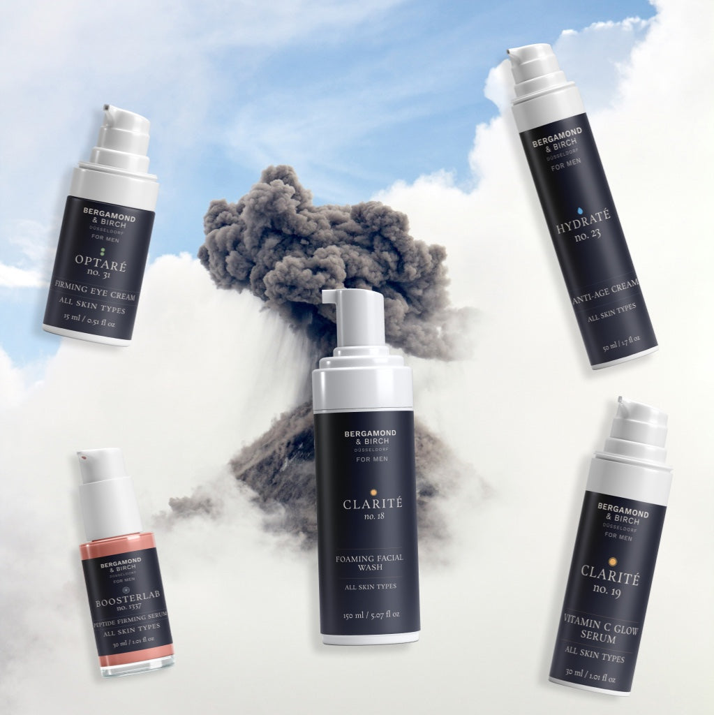 Produktcollage von Bergamond & Birch Skincare – Clarité Facial Wash, Hydraté Anti-Age Cream, Optaré Eye Cream, BoosterLab Serum und Clarité Vitamin C Glow Serum – arrangiert vor einer aufsteigenden Vulkanwolke.