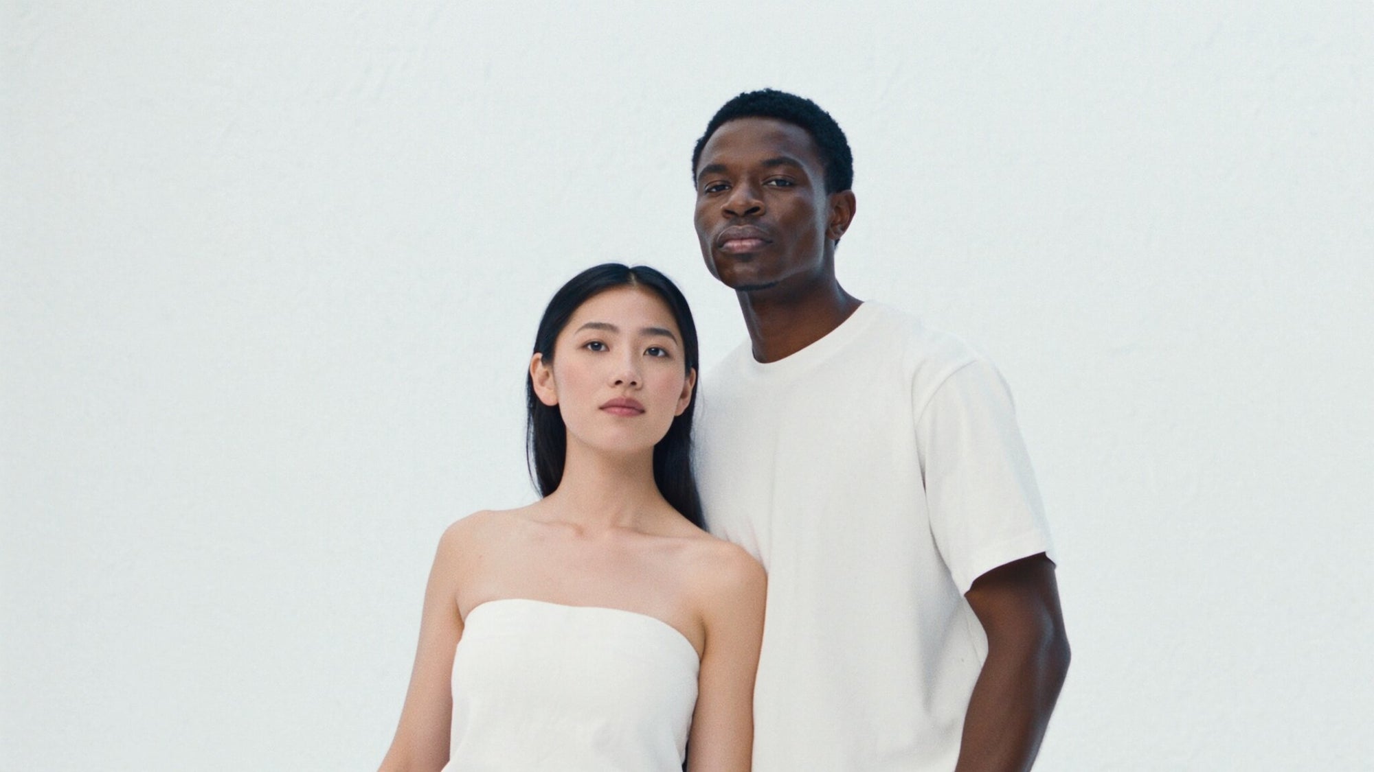 Zwei Personen stehen dicht beieinander vor reinweißem Hintergrund, eine trägt ein schulterfreies weißes Top, die andere ein weißes T‑Shirt – minimalistisches Portrait‑Duo, das die Klarheit und Vielfalt der BERGAMOND & RICH Hautpflege widerspiegelt.
