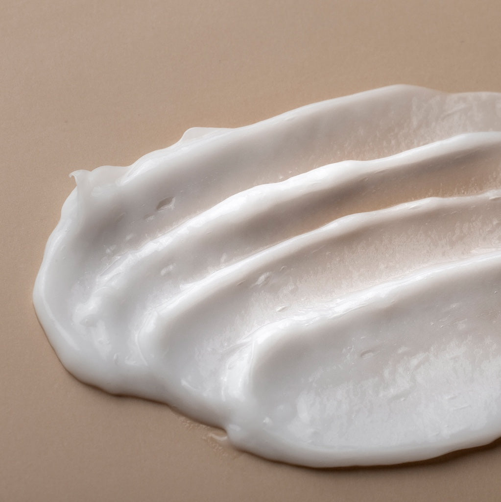 Nahaufnahme einer weißen Cremetextur, gleichmäßig in sanften Linien über einen beigen Untergrund gestrichen.