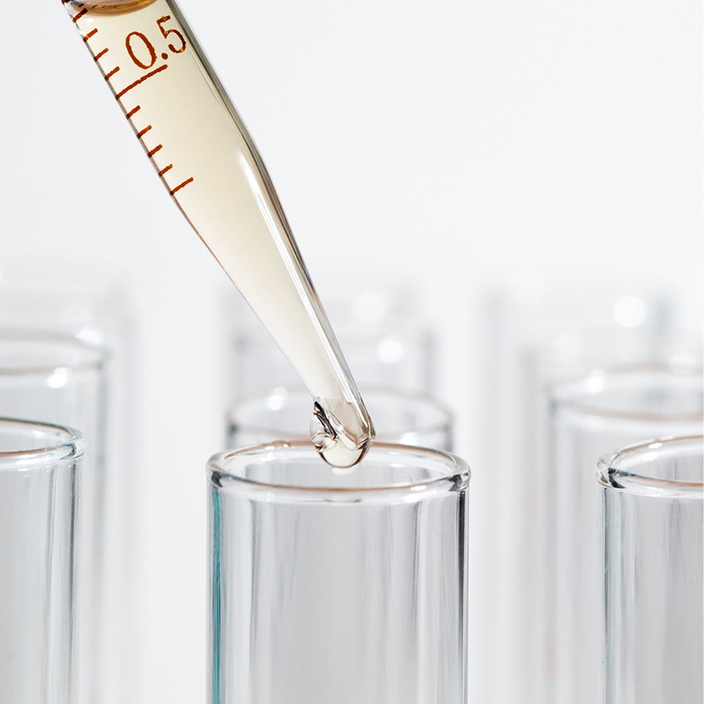 Pipette mit transparenter Flüssigkeit, die in ein Glasröhrchen im Labor getropft wird.